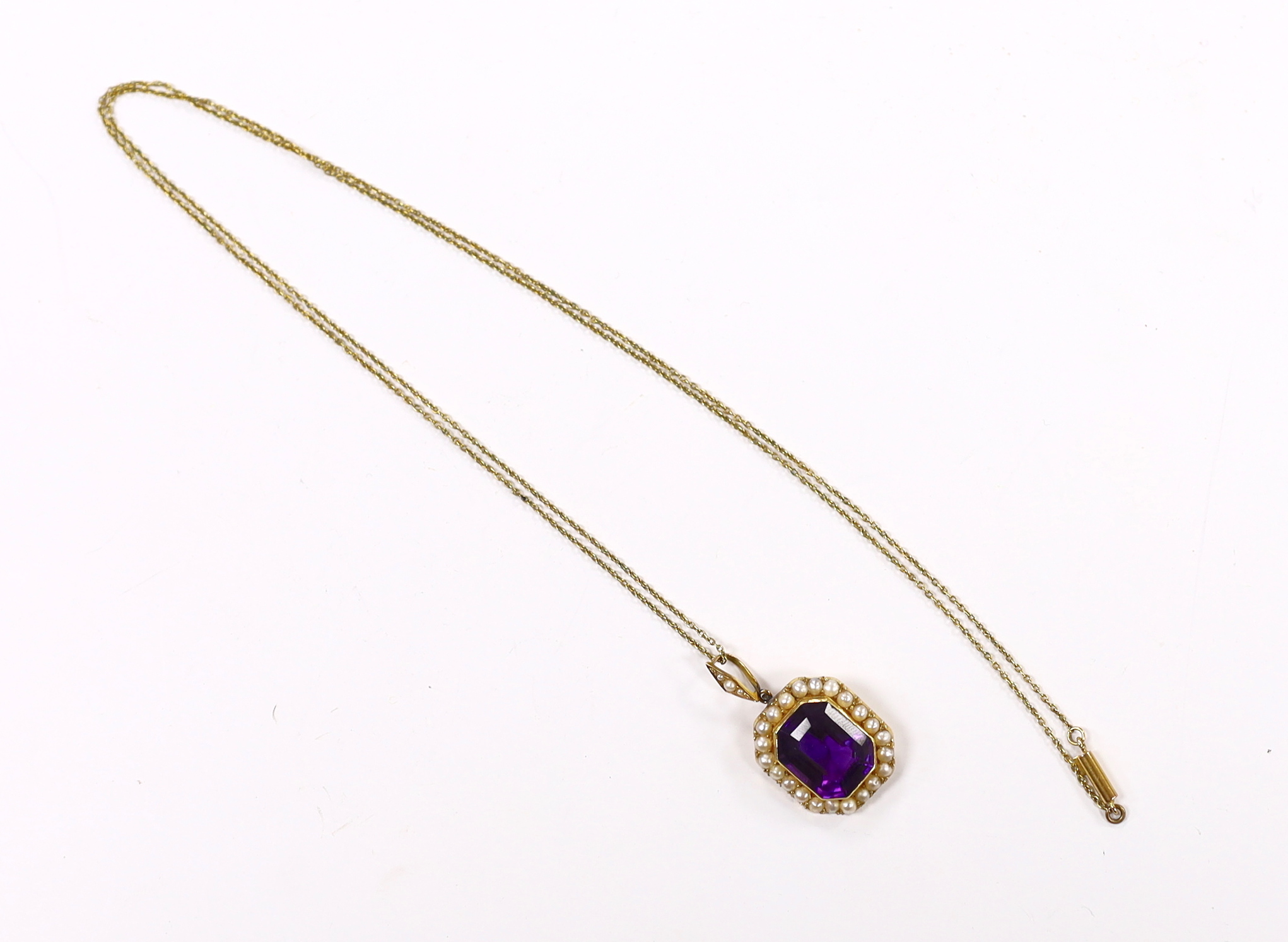 An Edwardian 15ct, amethyst and seed pearl cluster set pendant, overall 33mm, on a 9ct chain, 70cm, chain, 2.5 grams.